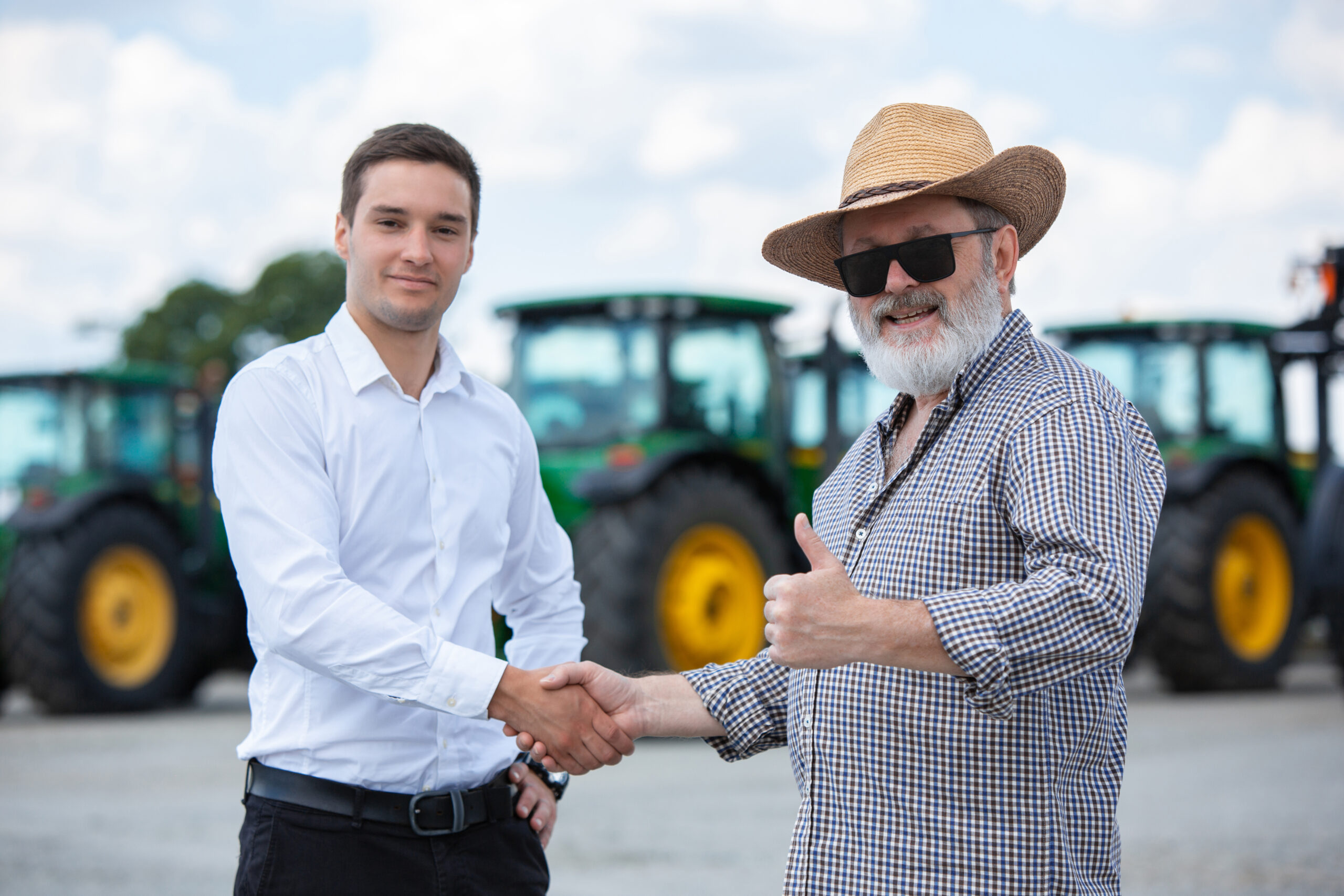 Professional farmer with a modern combine at field in sunlight at work. Confident, bright summer colors. Agriculture, exhibition, machinery, plant production. Senior man near his tractor with investor.